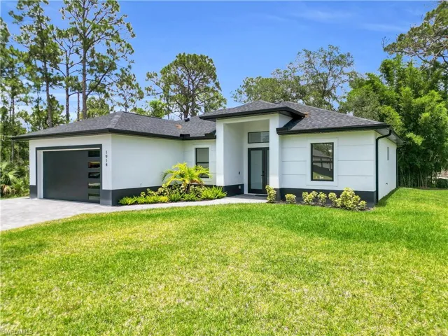 Prairie-style house with a front lawn, an attached garage, decorative driveway, and stucco siding
