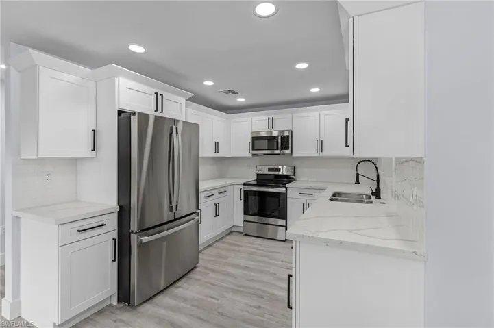Kitchen with appliances with stainless steel finishes, recessed lighting, white cabinetry, and light stone counters