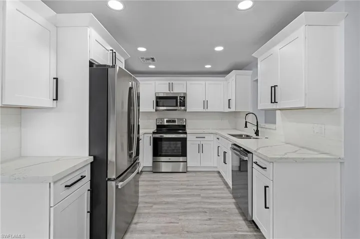 Kitchen with stainless steel appliances, white cabinetry, backsplash, and recessed lighting