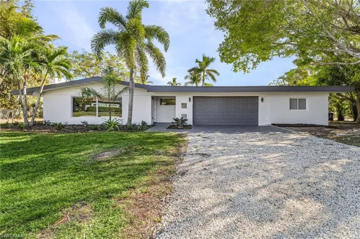 View of front of house featuring a garage, stucco siding, and gravel driveway