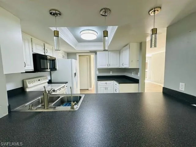 Kitchen featuring a tray ceiling, white appliances, pendant lighting, and white cabinetry