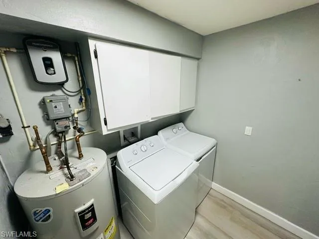 Laundry area featuring light hardwood / wood-style flooring, washer and clothes dryer, water heater, and cabinets