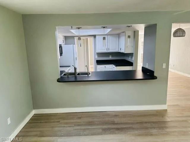 Kitchen featuring sink, white refrigerator, decorative light fixtures, light hardwood / wood-style floors, and white cabinets