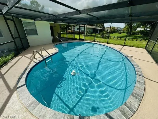 View of pool featuring glass enclosure, a lawn, and a patio