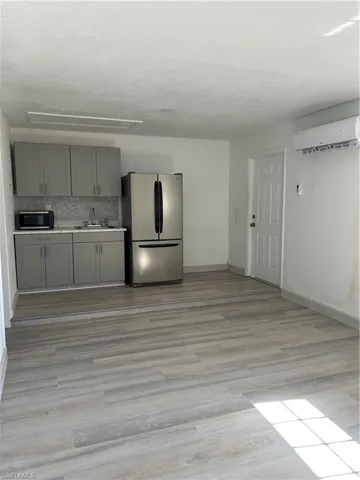 Kitchen with light hardwood / wood-style floors, decorative backsplash, stainless steel refrigerator, sink, and an AC wall unit