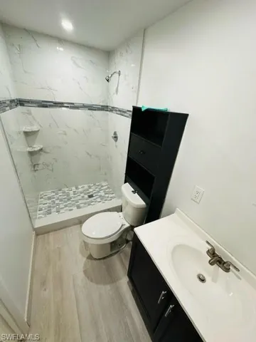 Bathroom featuring toilet, tiled shower, hardwood / wood-style floors, and vanity