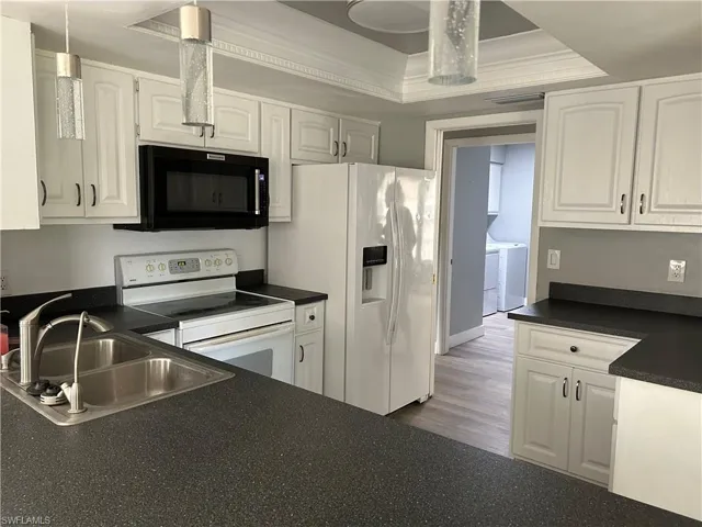 Kitchen with white cabinetry, separate washer and dryer, wood-type flooring, a tray ceiling, and white appliances