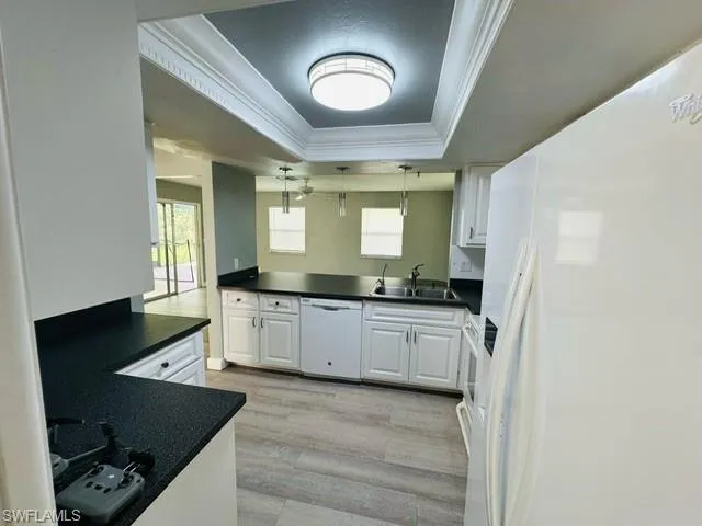 Kitchen with white cabinetry, sink, pendant lighting, a tray ceiling, and white appliances