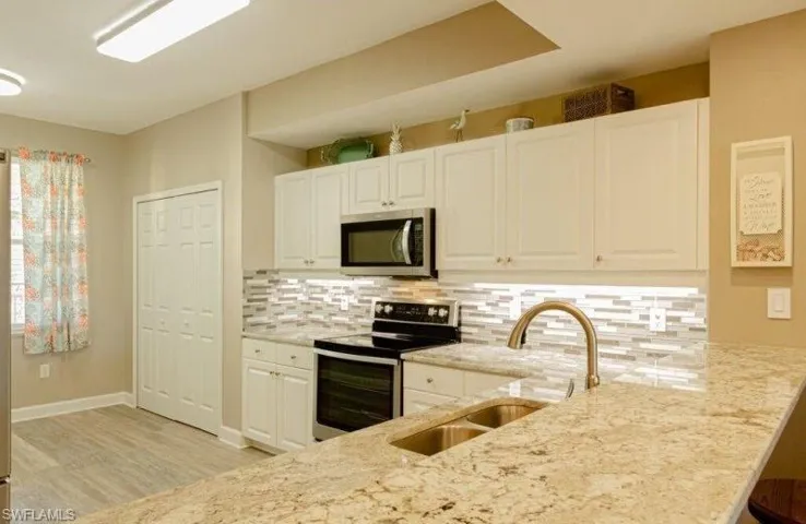 Kitchen with stainless steel appliances, light stone counters, white cabinetry, tasteful backsplash, and a breakfast bar area