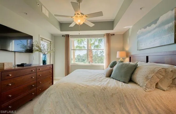 Bedroom featuring a tray ceiling, ceiling fan, multiple windows, and light colored carpet