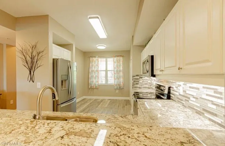 Kitchen with stainless steel appliances, light wood-style floors, white cabinetry, tasteful backsplash, and light stone counters