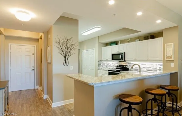 Kitchen with light stone counters, stainless steel appliances, a peninsula, a breakfast bar, and tasteful backsplash