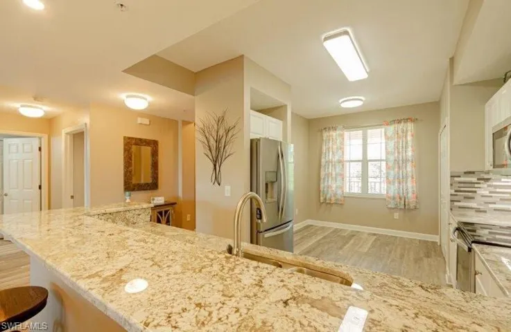 Kitchen featuring stainless steel appliances, a kitchen bar, light stone countertops, light wood-type flooring, and white cabinets