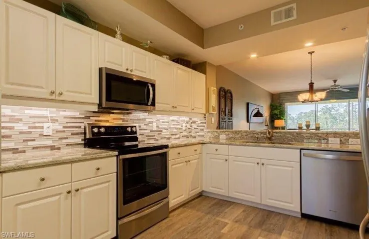 Kitchen featuring stainless steel appliances, white cabinetry, hanging light fixtures, and light stone counters