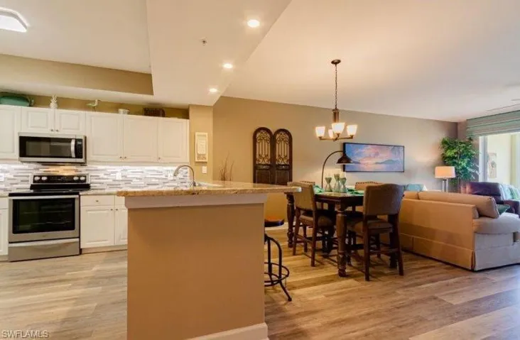 Kitchen with stainless steel appliances, open floor plan, white cabinets, a center island with sink, and light wood finished floors