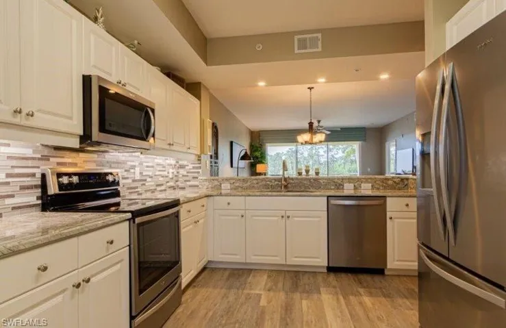 Kitchen with stainless steel appliances, white cabinetry, light wood-style flooring, and pendant lighting