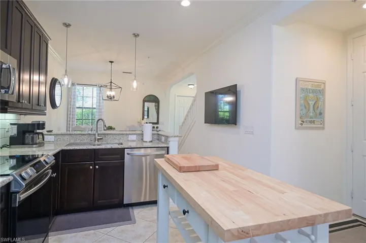 Kitchen with sink, butcher block countertops, dark brown cabinetry, appliances with stainless steel finishes, and light tile patterned floors