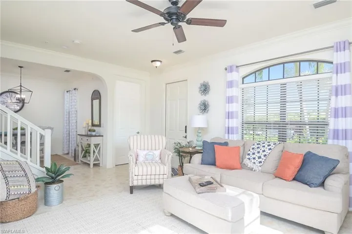 Tiled living room with ceiling fan with notable chandelier and ornamental molding