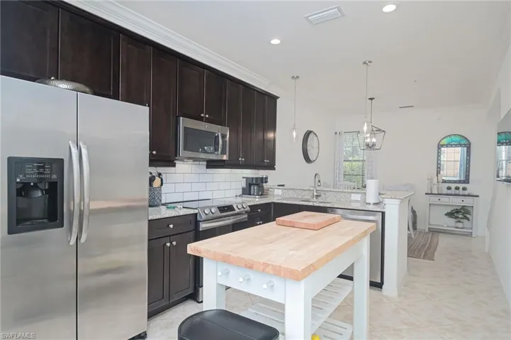 Kitchen with appliances with stainless steel finishes, decorative backsplash, light tile patterned flooring, a center island, and ornamental molding