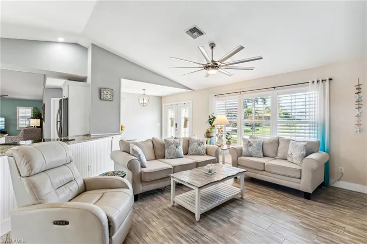Living room with ceiling fan with notable chandelier, light wood-type flooring, lofted ceiling, and french doors