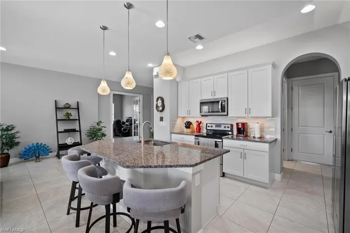 Kitchen featuring white cabinetry, sink, dark stone countertops, a kitchen island with sink, and appliances with stainless steel finishes