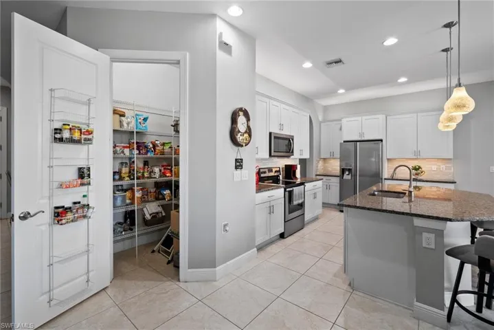 Kitchen with sink, stainless steel appliances, dark stone countertops, a center island with sink, and white cabinets