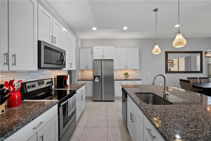 Kitchen with decorative backsplash, stainless steel appliances, sink, decorative light fixtures, and white cabinetry