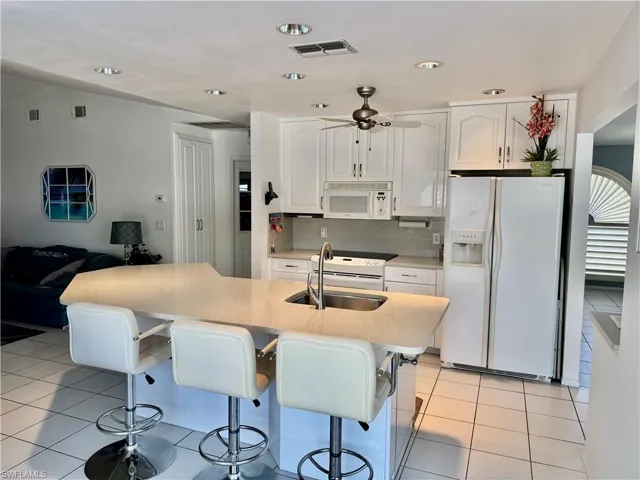 Kitchen featuring light tile patterned floors, white appliances, a kitchen breakfast bar, white cabinetry, and quartz countertops