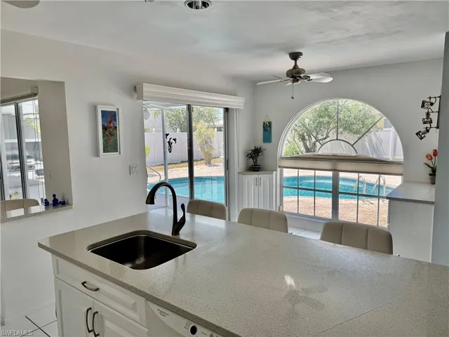 Kitchen with a ceiling fan, white cabinets, light stone counters, dishwasher, and a sink