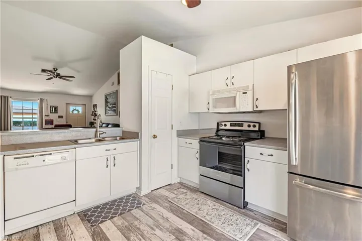 Kitchen featuring appliances with stainless steel finishes, a ceiling fan, lofted ceiling, white cabinetry, and light wood-style flooring