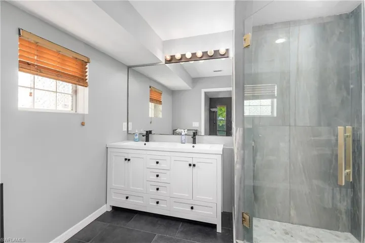 Bathroom featuring a stall shower, double vanity, and dark tile patterned floors