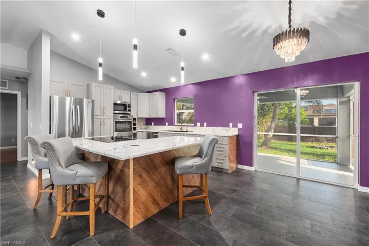 Kitchen with vaulted ceiling, stainless steel appliances, light stone countertops, hanging light fixtures, and a kitchen breakfast bar