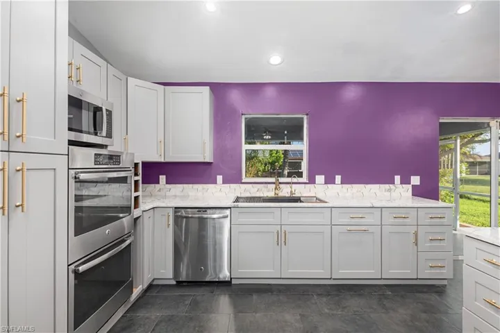 Kitchen featuring stainless steel appliances, light stone countertops, gray cabinetry, recessed lighting, and dark tile patterned floors