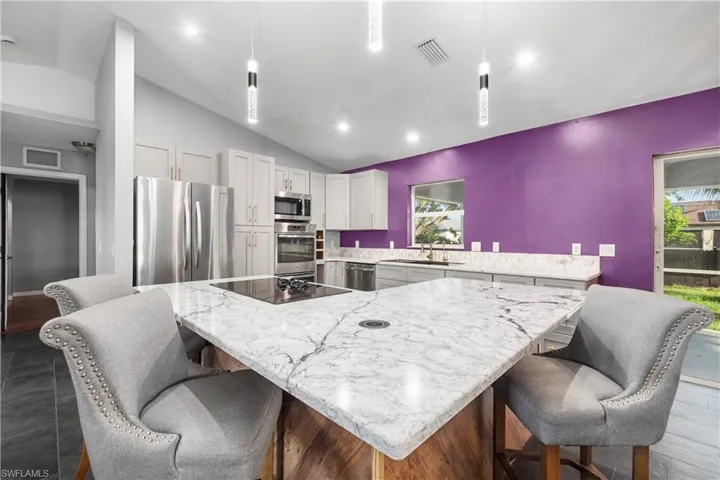 Kitchen with vaulted ceiling, pendant lighting, a kitchen bar, stainless steel appliances, and light stone counters