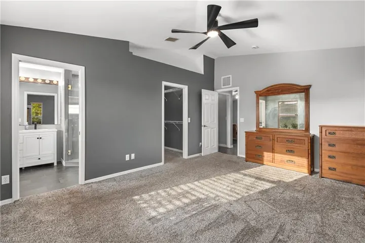 Unfurnished bedroom featuring a walk in closet, carpet floors, a ceiling fan, and ensuite bath