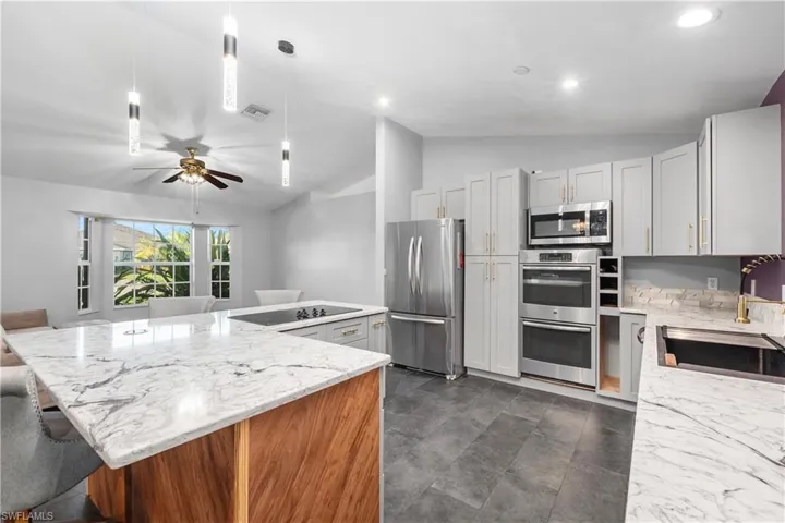 Kitchen with vaulted ceiling, light stone countertops, stainless steel appliances, a breakfast bar, and ceiling fan