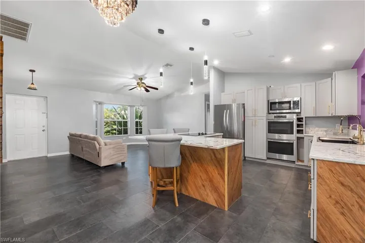 Kitchen featuring vaulted ceiling, light stone countertops, open floor plan, hanging light fixtures, and a ceiling fan