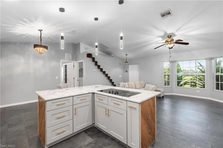 Kitchen with light stone counters, vaulted ceiling, a center island, decorative light fixtures, and open floor plan