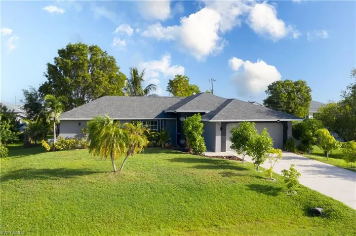 Ranch-style home featuring a front lawn, roof with shingles, driveway, an attached garage, and stucco siding