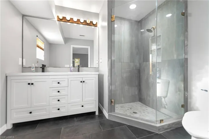 Bathroom with a stall shower, double vanity, and dark tile patterned flooring