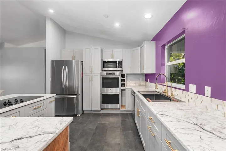 Kitchen featuring light stone countertops, stainless steel appliances, vaulted ceiling, gray cabinets, and recessed lighting