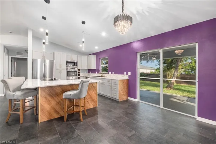 Kitchen with vaulted ceiling, a kitchen breakfast bar, a center island, stainless steel appliances, and light stone counters