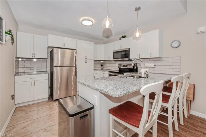 Kitchen with appliances with stainless steel finishes, white cabinetry, hanging light fixtures, and backsplash