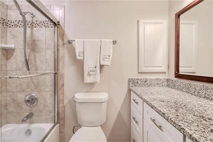 Full bathroom with enclosed tub / shower combo, vanity, and toilet