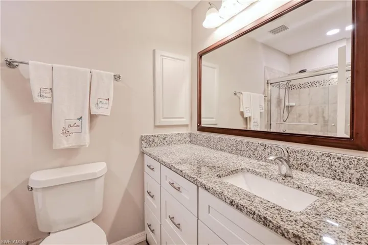 Bathroom with a shower with shower door, vanity with extensive cabinet space, and toilet