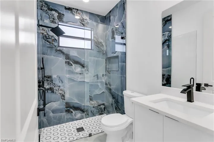 Full bathroom featuring a marble finish shower, vanity, and toilet