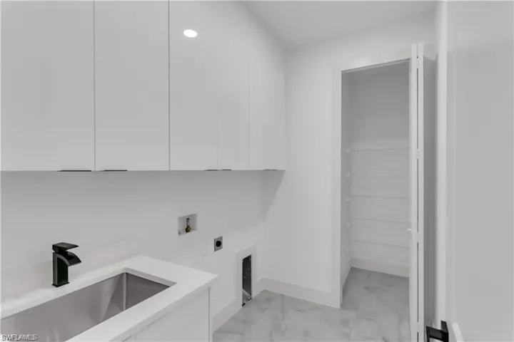 Washroom featuring cabinet space, light marble finish floors, electric dryer hookup, washer hookup, and baseboards