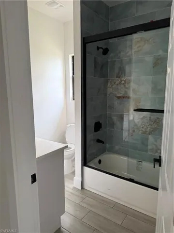 Bathroom with vanity, enclosed tub / shower combo, and wood finish floors