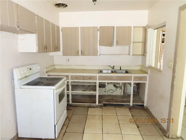 Kitchen with white electric range, light countertops, light tile patterned floors, and cream cabinetry