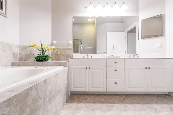 Bathroom with double vanity, light tile patterned floors, and a bath